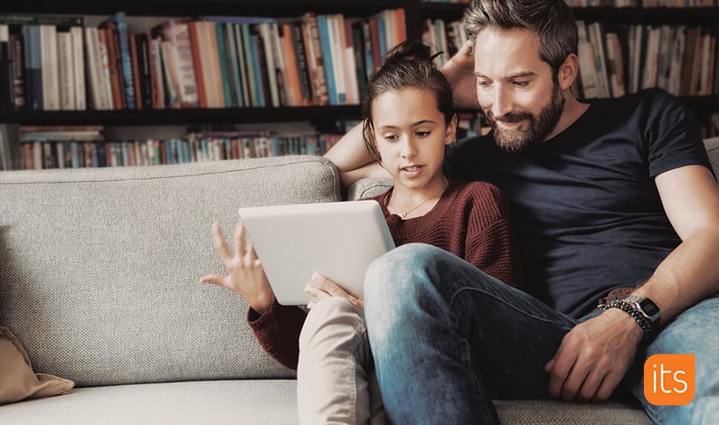 Far og datter sidder i sofaen i deres stue, mens de kigger på en tablet sammen.