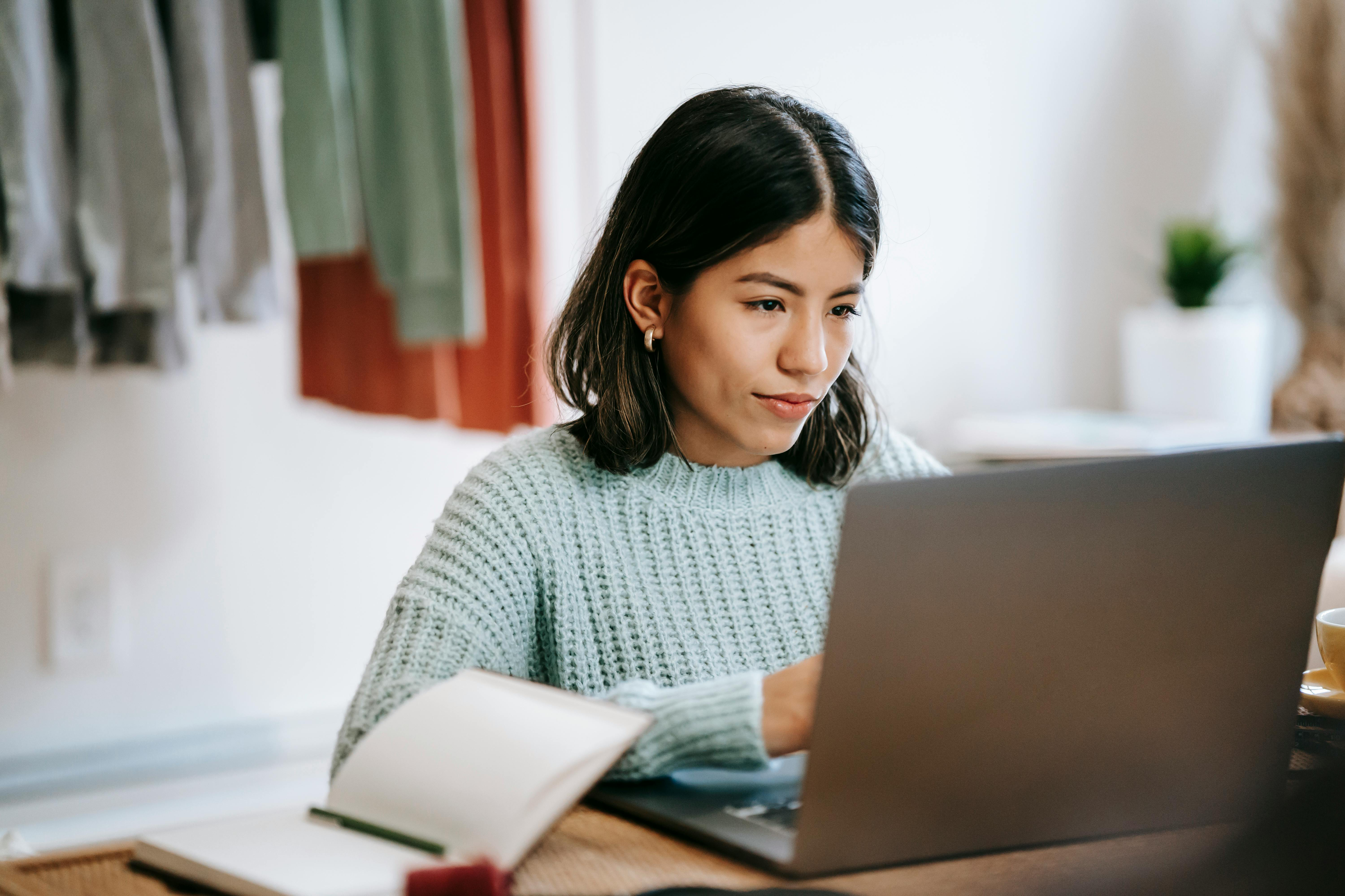 kvindelig studerende med sort hår og en blå trøje sad foran en bærbar computer